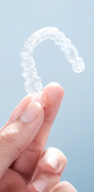 Dentist Flushing NY Close-Up of Someone Holding Invisalign Retainer in their Fingers Close-Up of Someone Holding Invisalign Retainer in their Fingers